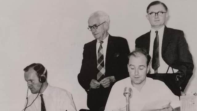 Two men sat down in front of mics, with two older men in suits stood behind them - black and white pic