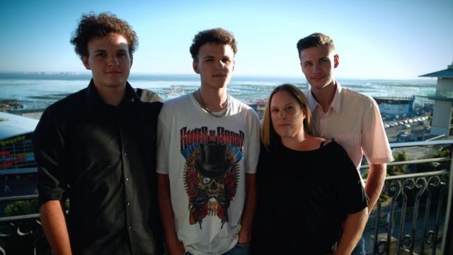 A middle-aged white woman standing with her three children in front of the sea