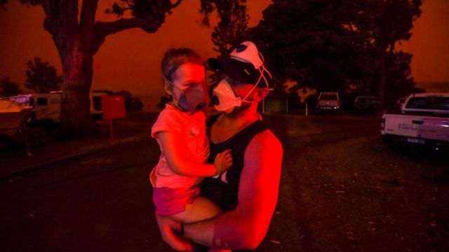 Un residente de Mallacoota sostiene a su hija con mascarillas en medio del humo.
