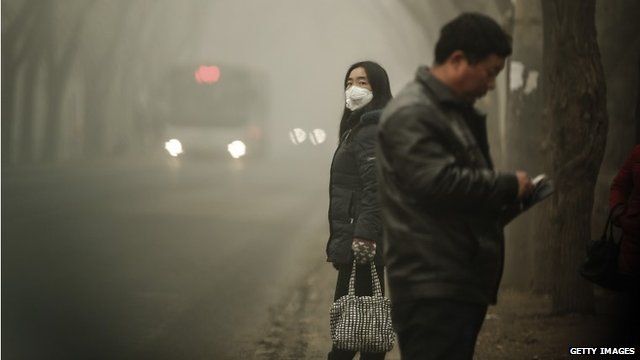 A woman wears a face mask next to traffic shrouded in heavy smog on December 1, 2015 in Beijing