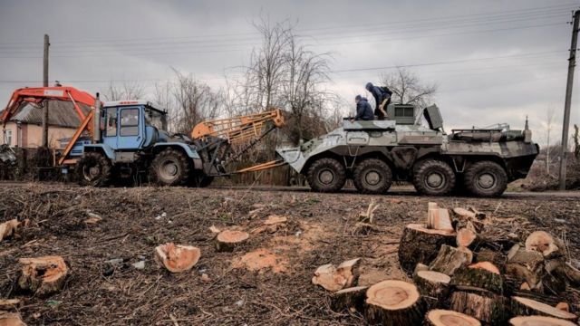 Украинцы на тракторе тянут трофейный бронетранспортер в окрестностях освобожденного от российских войск города Тростянец