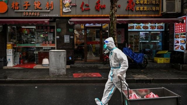 A worker covered head to foot in a white protective suit pulls a cart with meat inside past restaurants