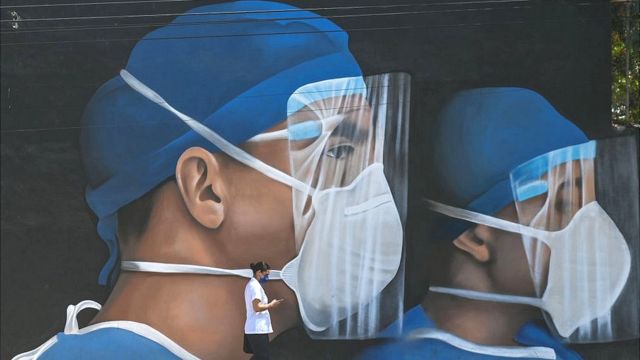 Homem passando por mural de profissionais de saúde usando equipamentos de proteção pessoal