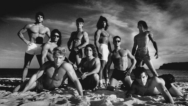 Imagem mostra homens musculosos sem camisa na praia