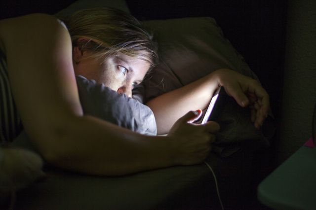 Mulher checando o celular à noite na cama 