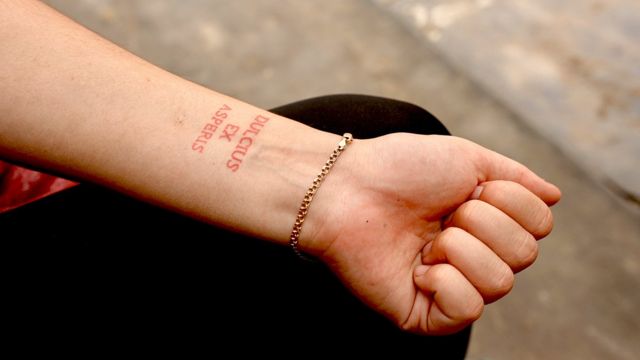 Tatuagem com inscrição em latim que diz "a doçura segue a dificuldade"