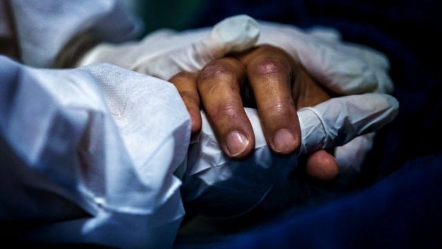 Un agent de santé portant un équipement de protection individuelle (EPI) tient la main d'un patient le 30 avril 2021dans un hôpital de Maricá, au Brésil