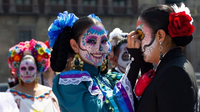 Mujeres se maquillan la cara en el desfile de Día de Muertos