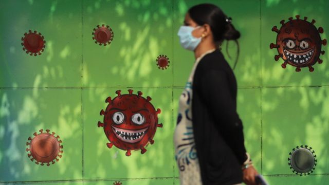 A woman wearing a mask as a preventive measure against the Covid-19 coronavirus walks past a mural in New Delhi.