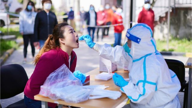 كان عامل طبي يرتدي ملابس واقية يجري اختبار كوفيد وأخذ عينات لامرأة في شنغهاي، الصين