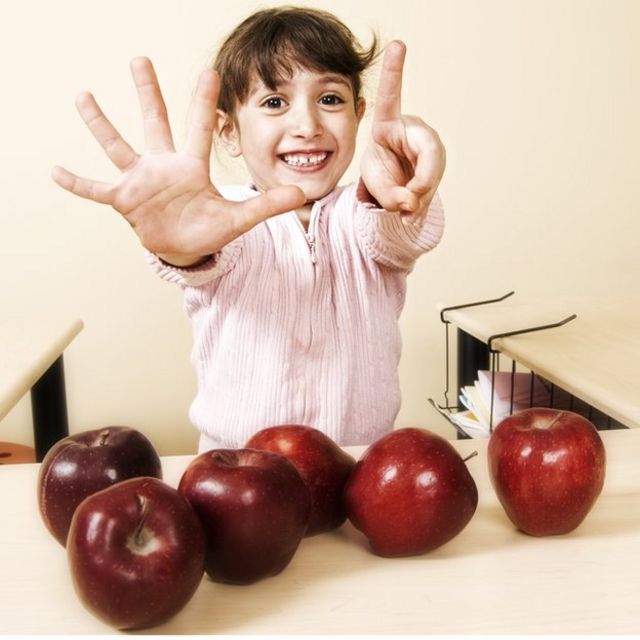 Niña mostrando cuántas manzanas hay con los dedos