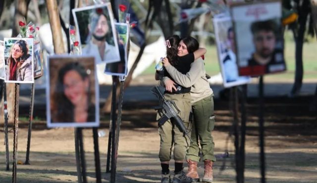 Soldados israelenses se abraçam enquanto olham fotos das vítimas do festival dos ataques de 7 de outubro