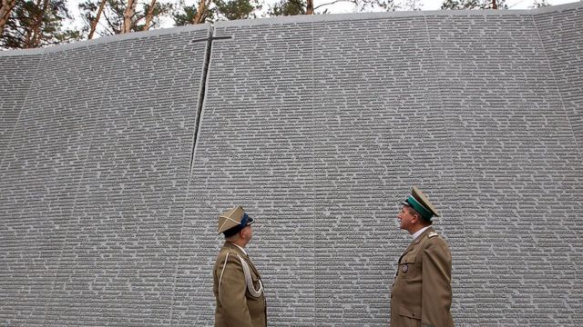 Soldados polacos parados frente a una pared con nombres de víctimas grabados en Bykivnia