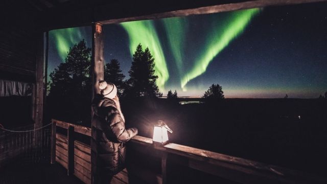 Mulher observa luzes da aurora boreal em varanda de casa