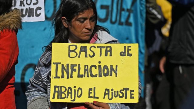 A woman holds a placard that reads Enough of inflation