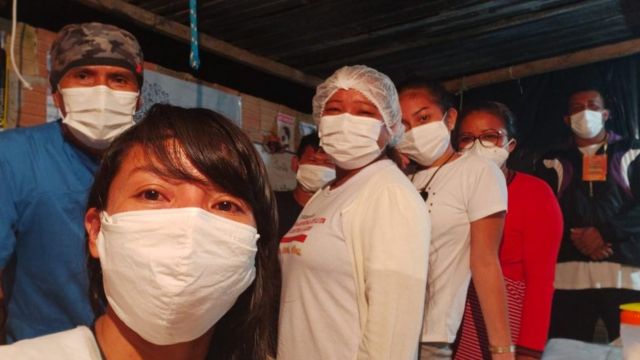 Vanda tira foto com outras seis pessoas de máscara, em ambiente interno