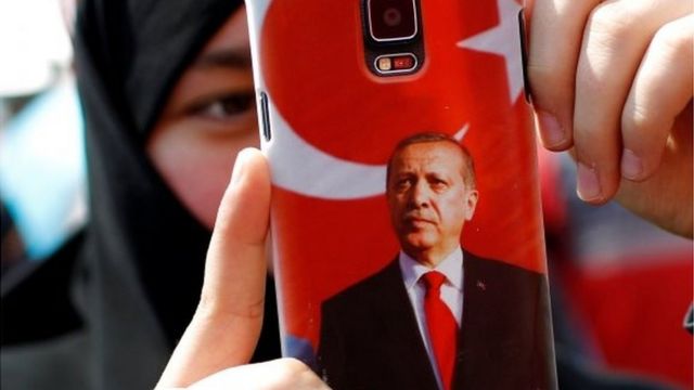Una mujer toma una foto con un celular decorado con la imagen de Erdogan.
