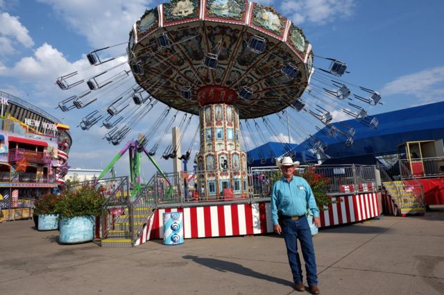 A man in a cowboy hat stands in front of a fair ride