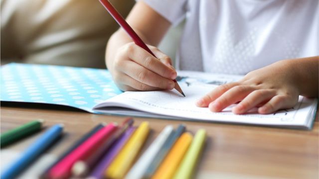 Criança escrevendo com lápis de cor em caderno
