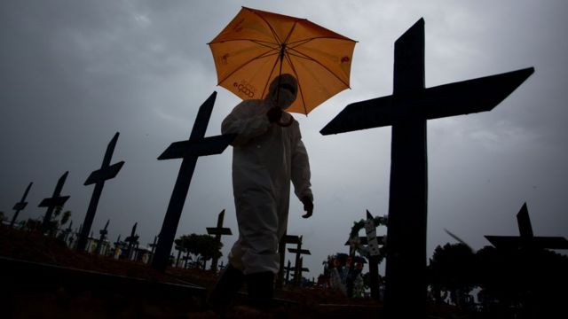Un trabajador con traje de proteccion recorre tumbas de victimas de covid-19 en Brasil.