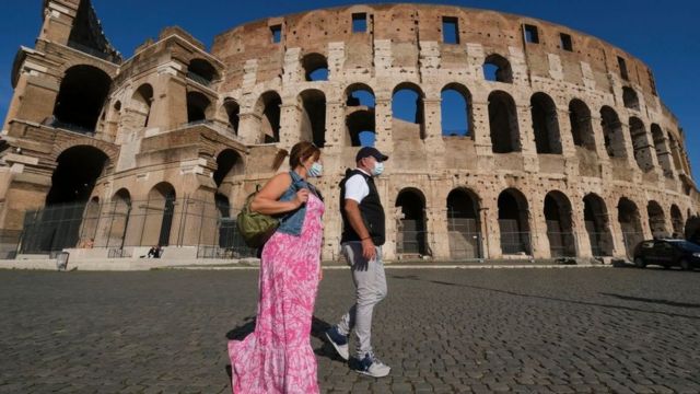 Dos personas con mascarilla frente al Coliseo de Roma.