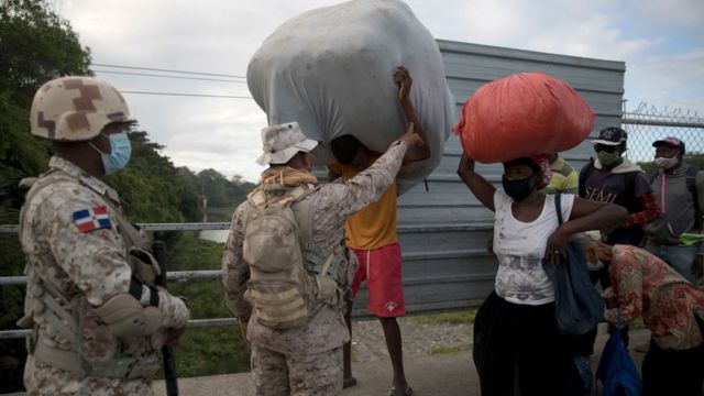 Portão de acesso à fronteira. Homens e mulheres com sacolas são revistados por soldados dominicanos