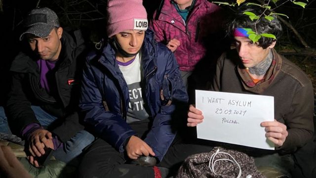 Мигранты из Ирака на границе Польши вскоре после того, как они пересекли границу из Беларуси. На плакате написано "прошу убежища".