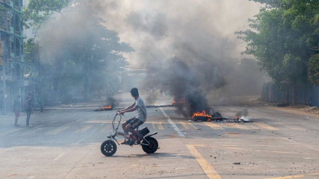 راكب دراجة نارية يمر بالقرب من إطارات محترقة في الشارع أثناء احتجاج على الانقلاب العسكري في ميانمار