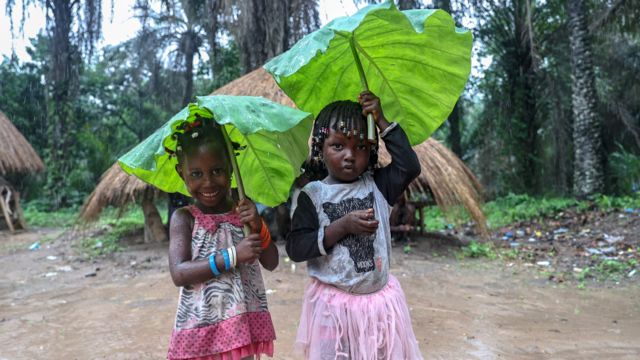 Children holding leaves to protect themselves from the rain pose in Boffa, Guinea - Sunday 25 July 2021