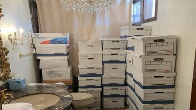 Boxes of papers are stacked in a bathroom with a chandelier and a toilet visible, at Mar-a-Lago