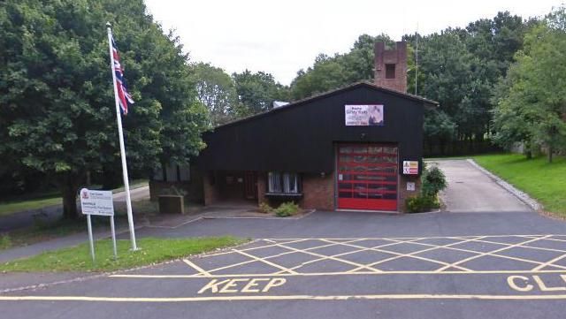 A small fire station with a bright red door and black façade. 