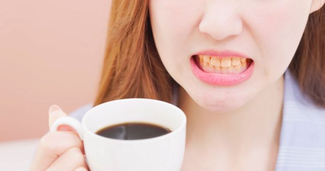 Mulher com dentes amarelados segurando xícara de café