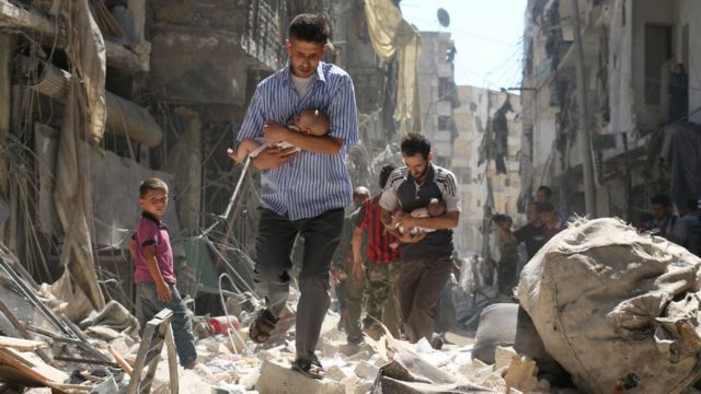 Hombres llevan bebés a través de los escombros de edificios destruidos en un ataque aéreo del gobierno en Alepo, Siria