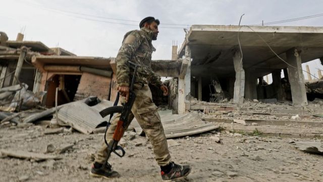 Combatiente sirio caminando por ciudad destrozada