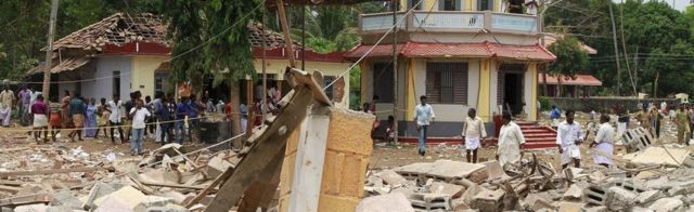 People stand next to debris after a broke out at a temple in Kollam in the southern state of Kerala, India