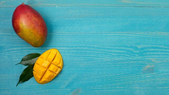 A whole mango and a half cut mango, on a blue wooden board