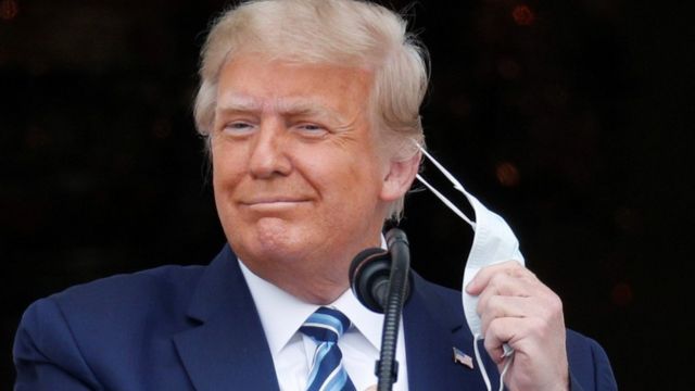 US President Donald Trump removes his mask as he steps out onto a White House balcony to speak to supporters gathered on the South Lawn for a campaign rally the White House is calling 