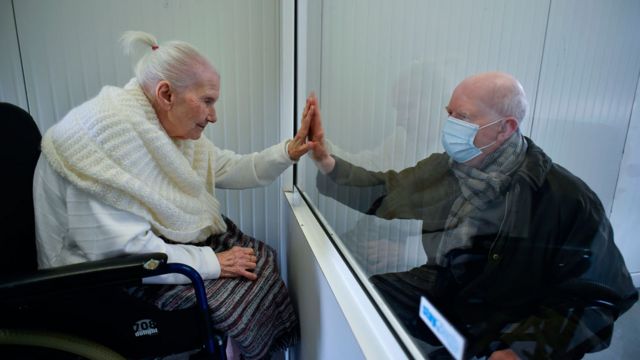 Una anciana infectada con covid-19 saluda a su hijo a través de un cristal de plexiglass en Bélgica.