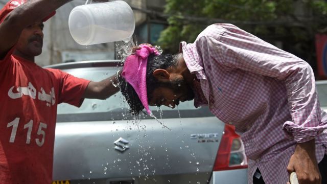 A man pours water on a pedestrian in a street on a hot summer day in Karachi, Pakistan.