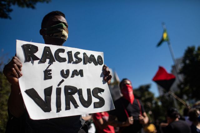 Homem com cartaz que diz 'Racismo é um vírus' durante protesto em São Paulo