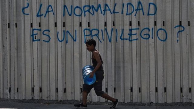 Un joven carga un bidón de agua por una calle de Caracas.