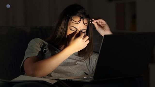 Mulher com feição preocupada em frente a laptop em ambiente escuro