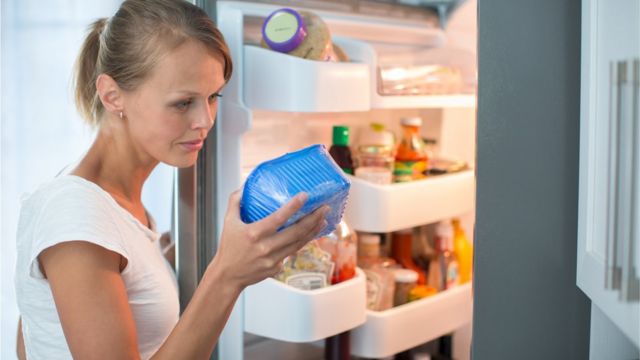 Uma mulher olha para um produto que ela tira da geladeira