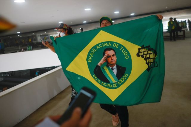 Pessoa dentro de prédio público com bandeira do Brasil alterada, mostrando foto de Bolsonaro no centro