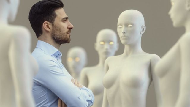 Hombre rodeado por robots de apariencia femenina.