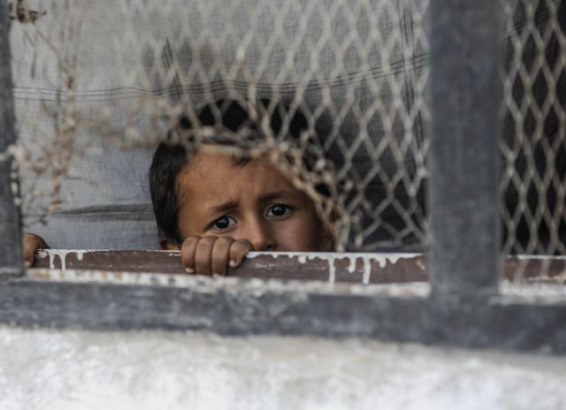 Un niño mira por la ventana de una ciudad siria azotada por la guerra.
