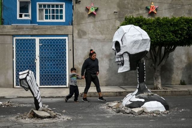 A woman and her child walk up to a cardboard skeleton in Mexico City