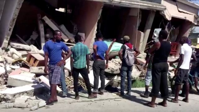 Personas observando un edificio derrumbado tras un terremoto, en Les Cayes, Haití.