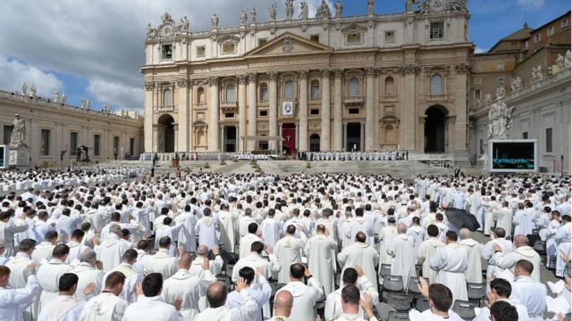 Diversos clérigos vestidos de branco enfileirados em cerimônia no pátio da Basílica de São Pedro
