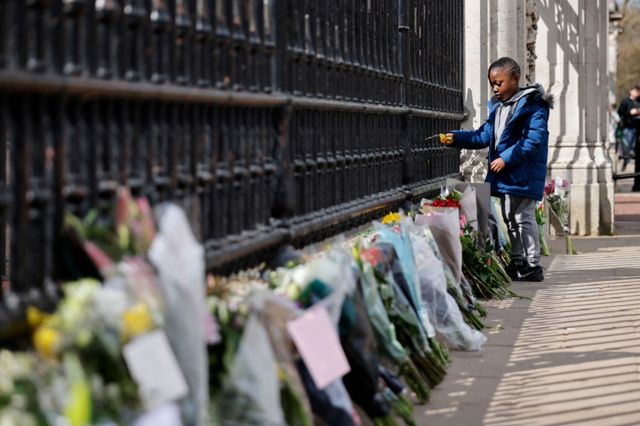 A boy adds to floral tributes against the railings at the front of Buckingham Palace